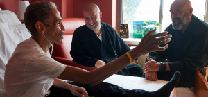 A patient in a hospital bed speaks with two contemplative caregivers.