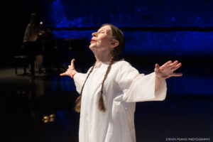 Meredith Monk performing onstage with her arms extended